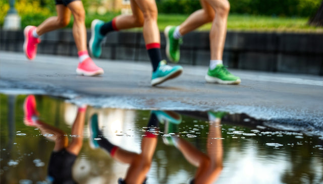 Runners' legs reflected in a puddle on the road.