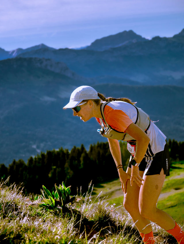 Athletic woman hiking a steep, grassy mountain trail.