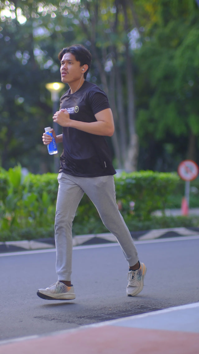 A young man jogging outdoors with a water bottle.